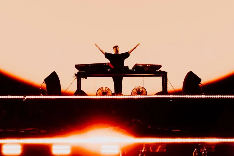 Silueta de DJ con brazos abiertos frente al atardecer